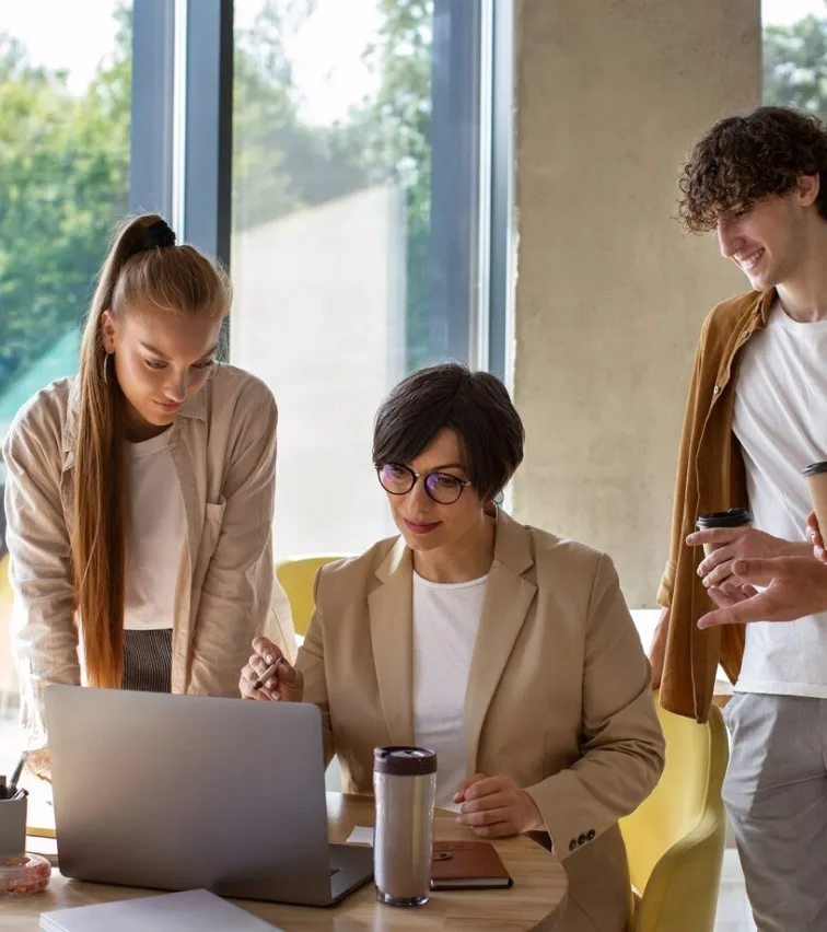 Three colleagues gathered around a laptop in a bright office